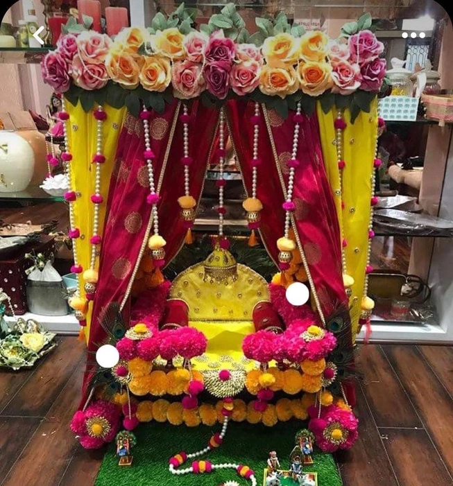 A beautifully crafted wooden swing (jhula) for Laddu Gopal Ji, adorned with a yellow and pink color combination and decorated with multi-colored flowers,